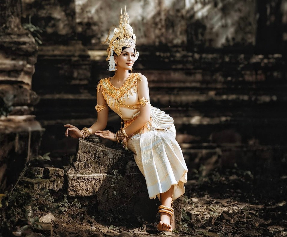 Thiếu nữ Khmer trong trang phục truyền thống với chiếc váy quấn và dải khăn vắt chéo vai trong khuôn viên chùa tháp thanh bình, dưới bóng dáng của những bức tượng Phật uy nghi. (Ảnh: Chú Râu) Thiếu nữ Khmer trong trang phục truyền thống với chiếc váy quấn và dải khăn vắt chéo vai trong khuôn viên chùa tháp thanh bình, dưới bóng dáng của những bức tượng Phật uy nghi. (Ảnh: Chú Râu)